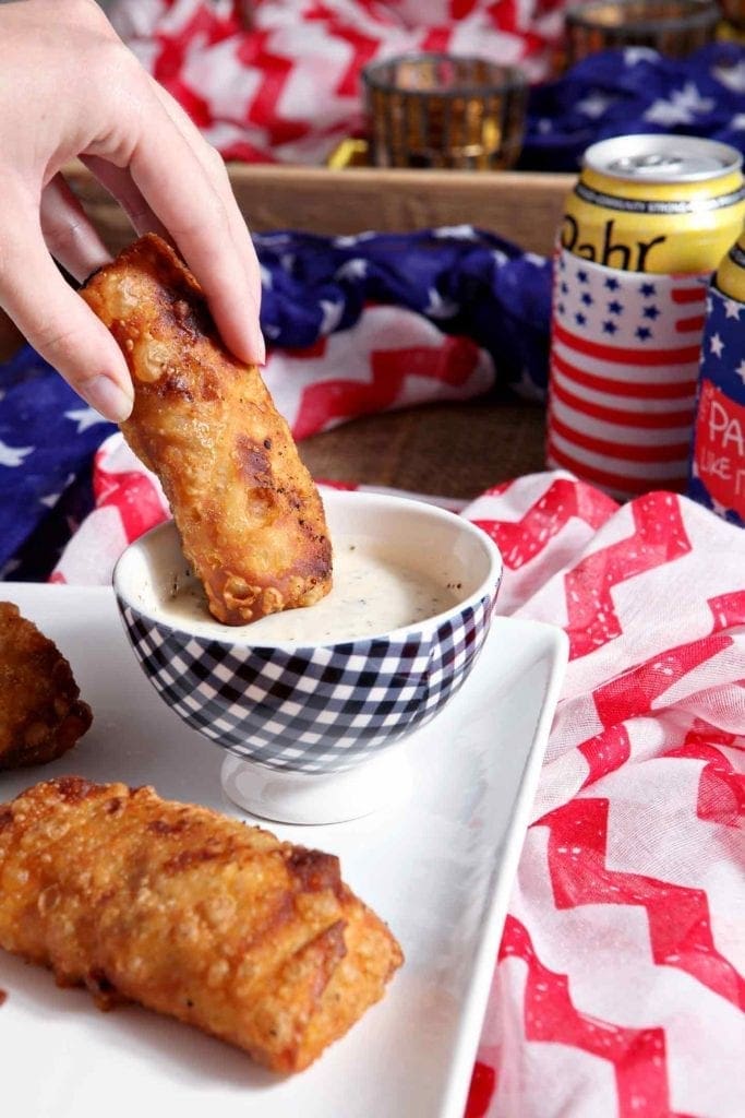 Hand dips Pulled Pork Coleslaw Eggrolls in bowl of dipping sauce