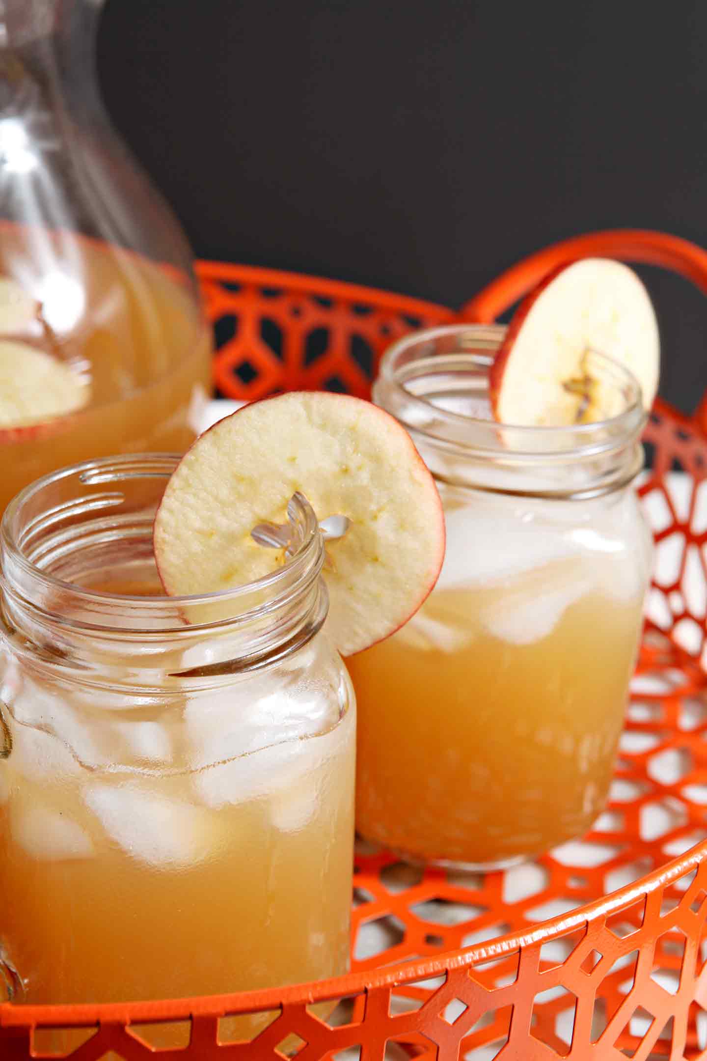 Close up of two glass jars holding orange drinks garnished with apple rounds