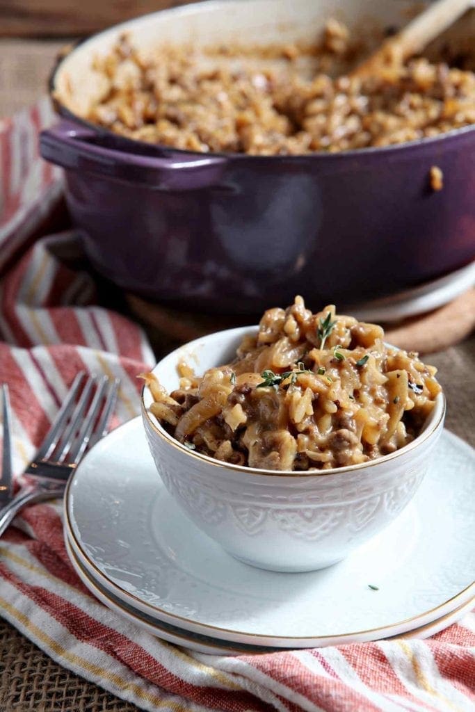 A small bowl of French Onion Risotto sits in front of a Dutch oven full of risotto