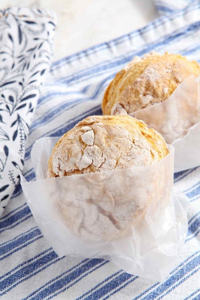 Two biscuits wrapped in parchment paper on linens 