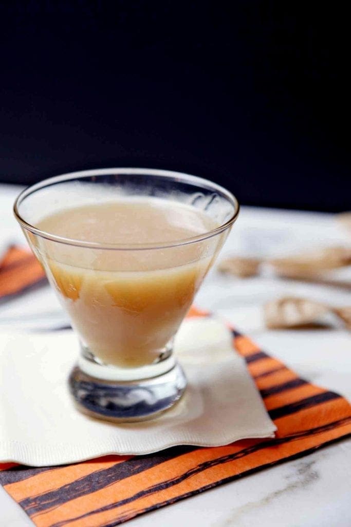 A Salted Caramel Appletini sits on a marble background, surrounded by salted caramels.