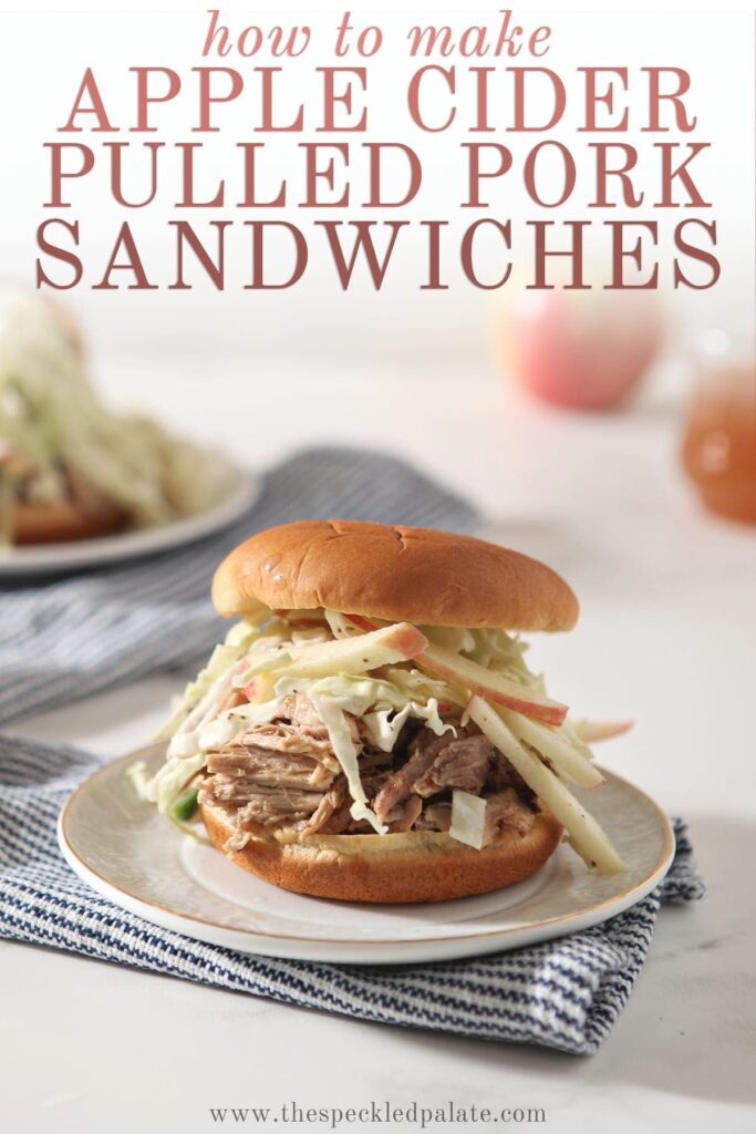 A white plate holds an Apple Cider Pulled Pork Sandwich on top of a blue striped towel with the text 'how to make apple cider pulled pork sandwiches'