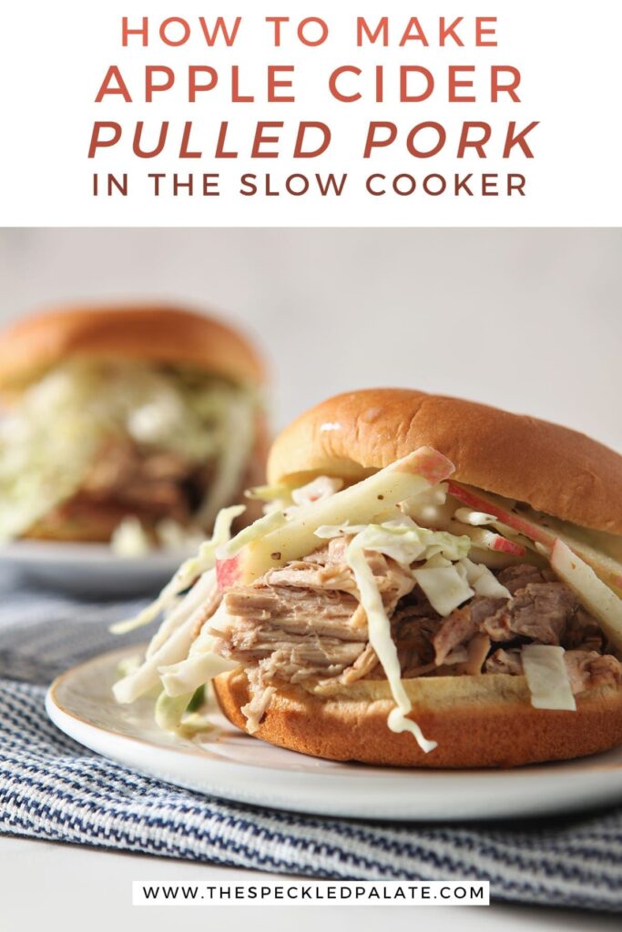 Close up of an Apple Cider Pulled Pork Sandwich with slaw on a white plate on top of a blue striped towel with the text 'how to make apple cider pulled pork in the slow cooker'