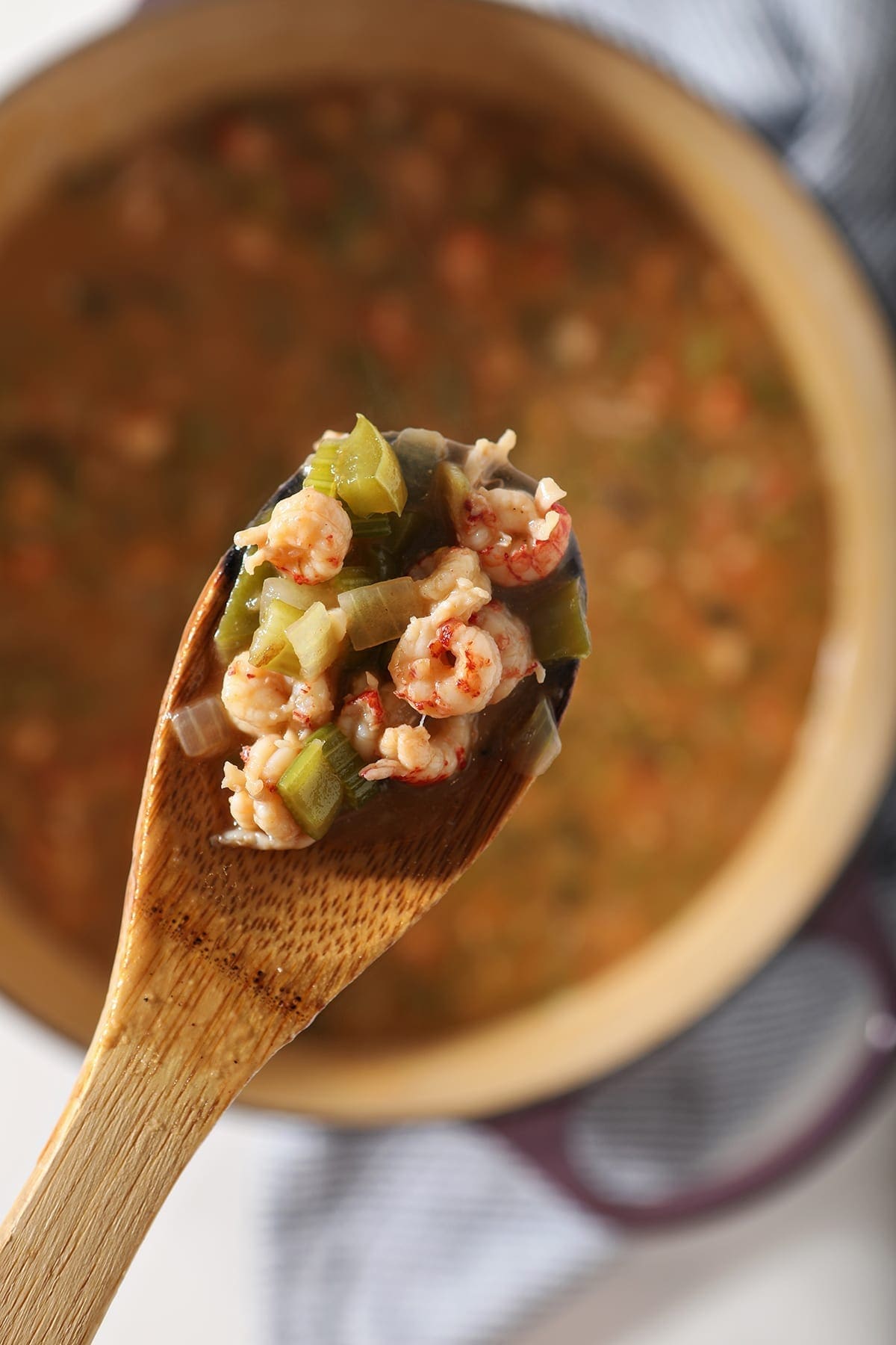 A wooden spoon holds crawfish tails and other etouffee ingredients