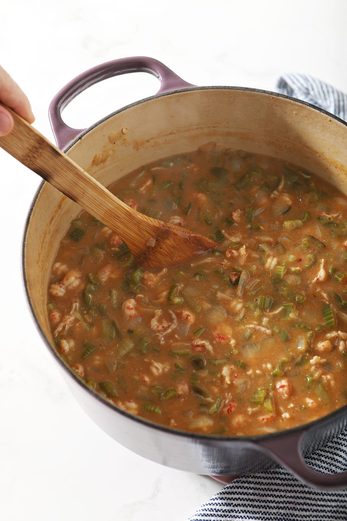 A wooden spoon stirs crawfish etouffee in a Dutch oven