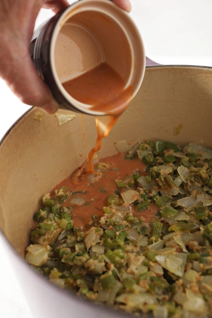 Orange crawfish fat is poured into a pot with sauteed vegetables