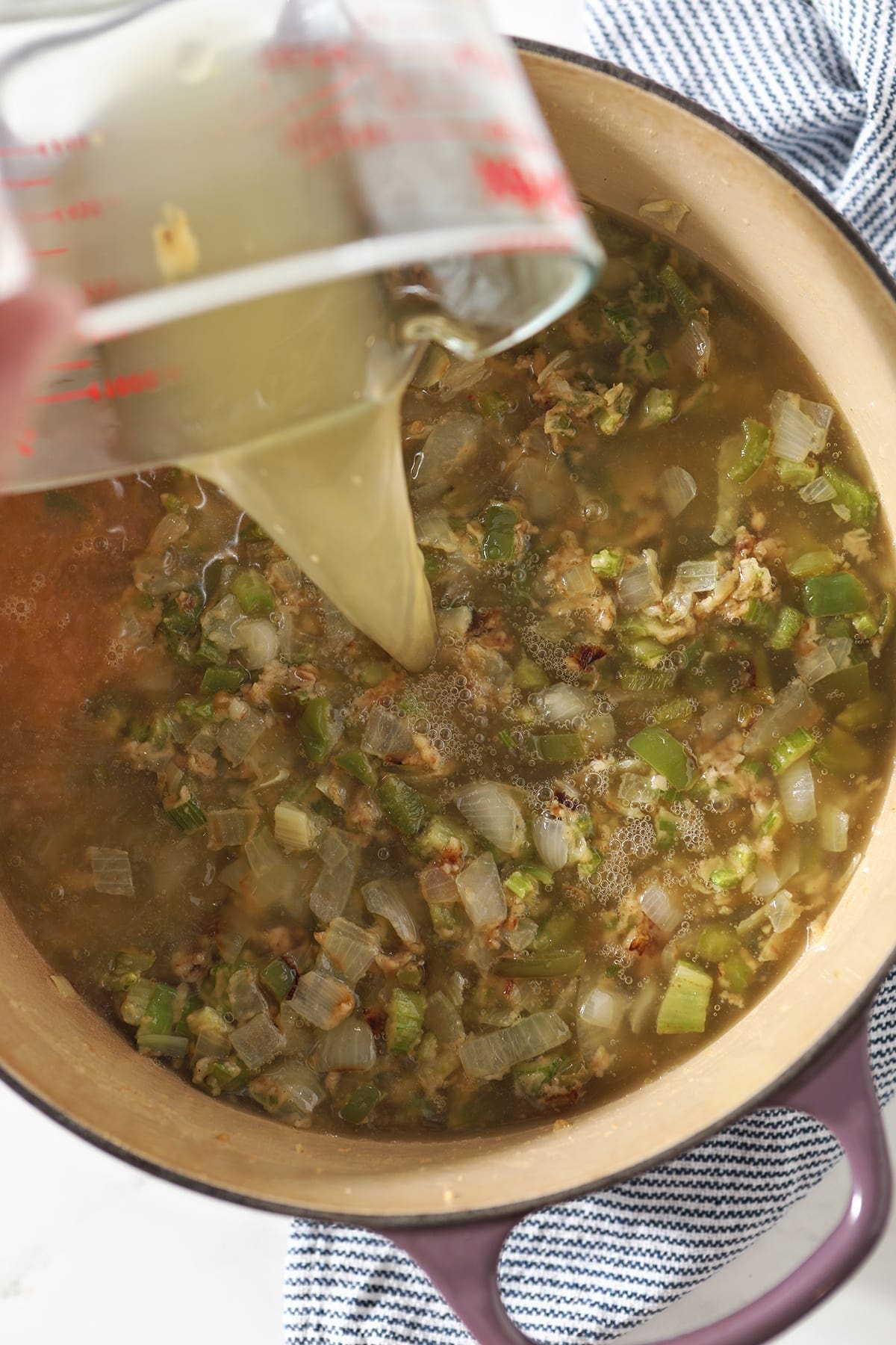 Chicken stock pours into a pot with vegetables