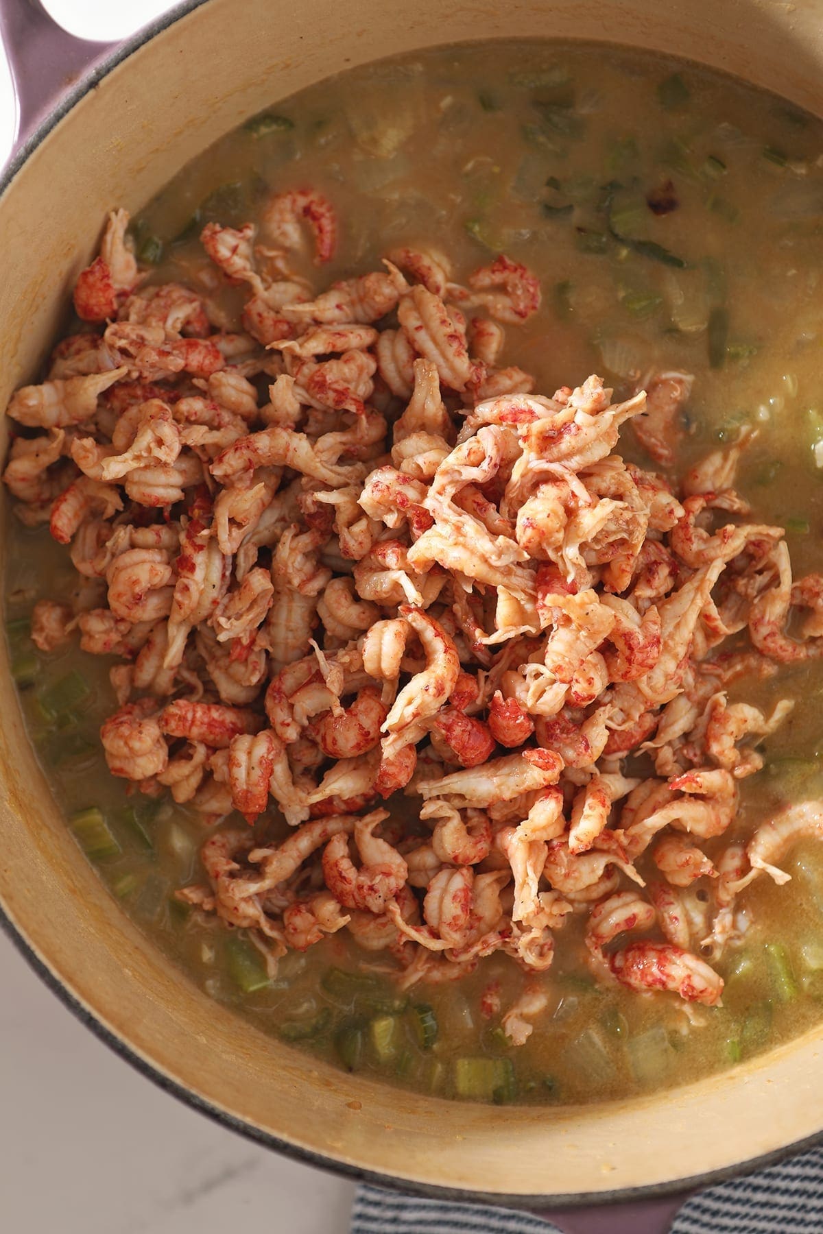 Crawfish tails sit on top of stewed vegetables in a Dutch oven