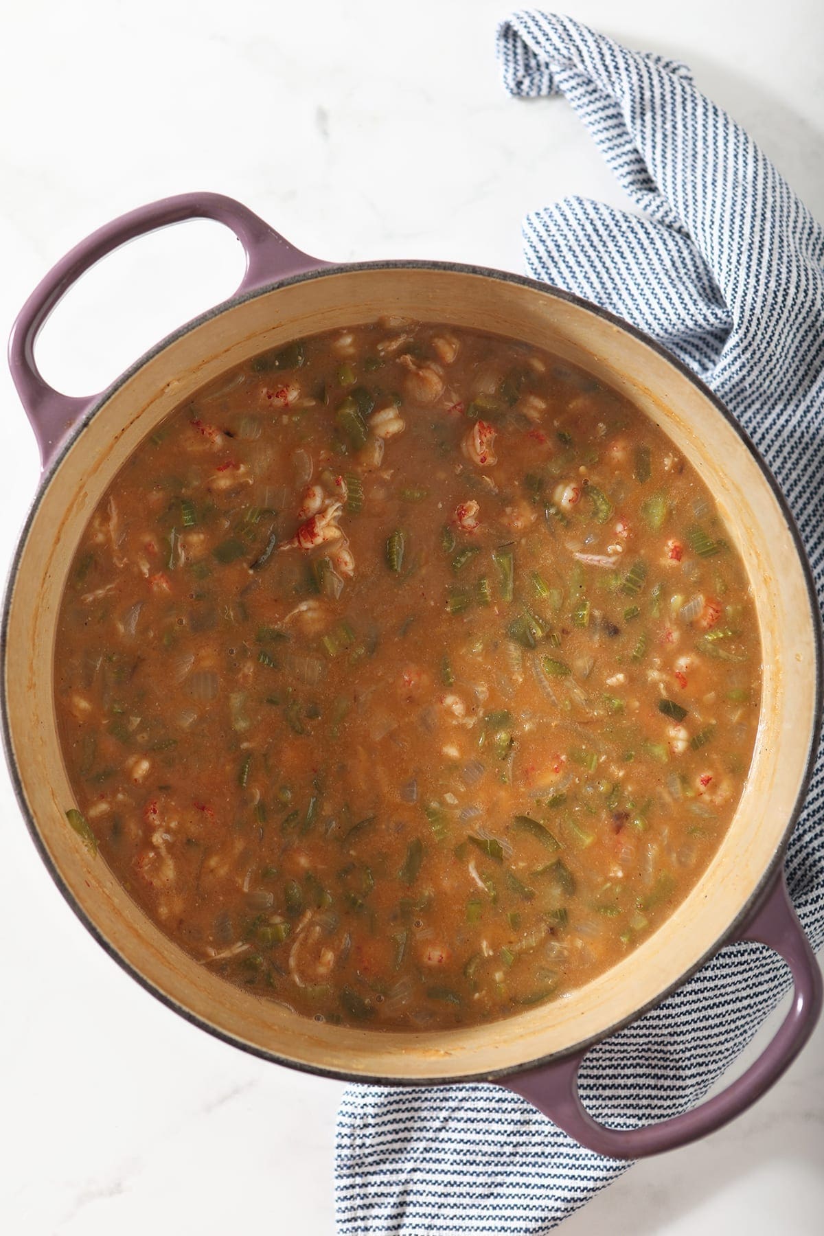 Crawfish etouffee in a purple Dutch oven, on top of a striped towel and marble