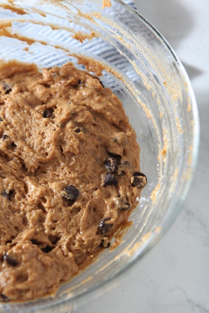 Muffin batter, with chocolate chips mixed in, sits in a bowl on a marble counter