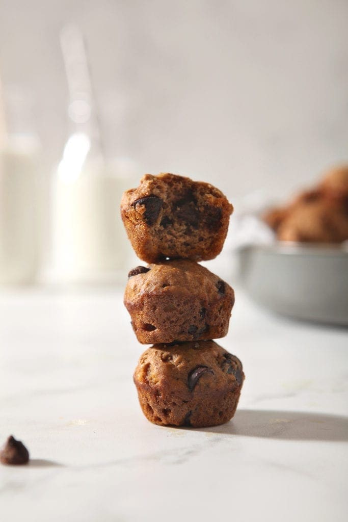 Three Mini Pumpkin Muffins with Chocolate Chips are stacked on top of each other, with milk bottles in the background