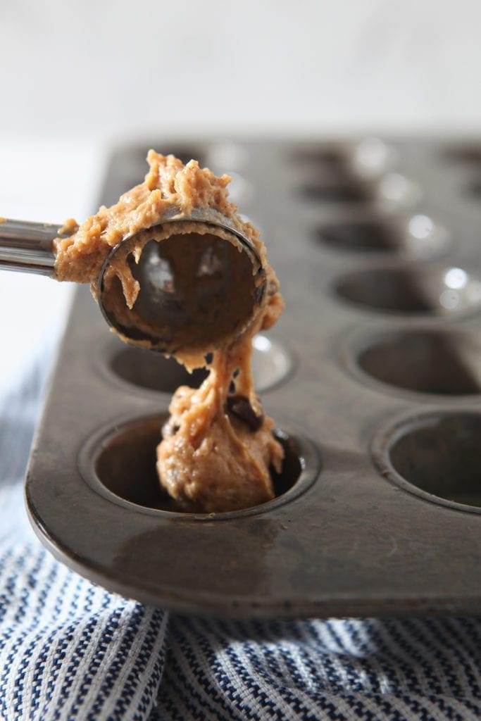 A cookie scoop dollops muffin batter into mini muffin tins