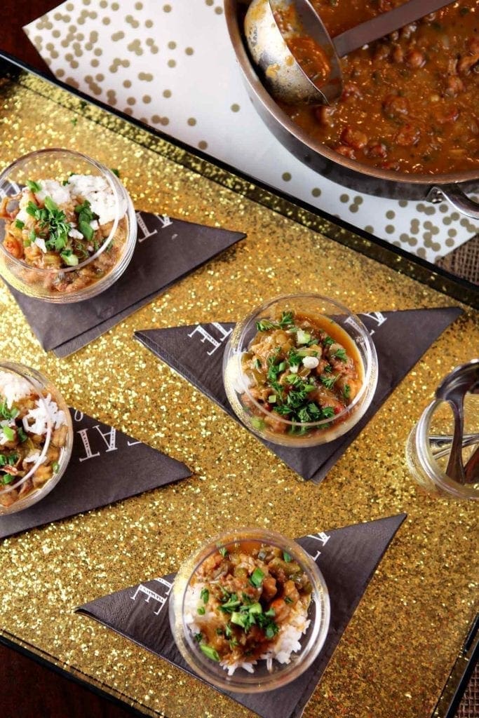 Overhead of four glasses holding crawfish etouffee garnished with parsley and green onions on a gold tray