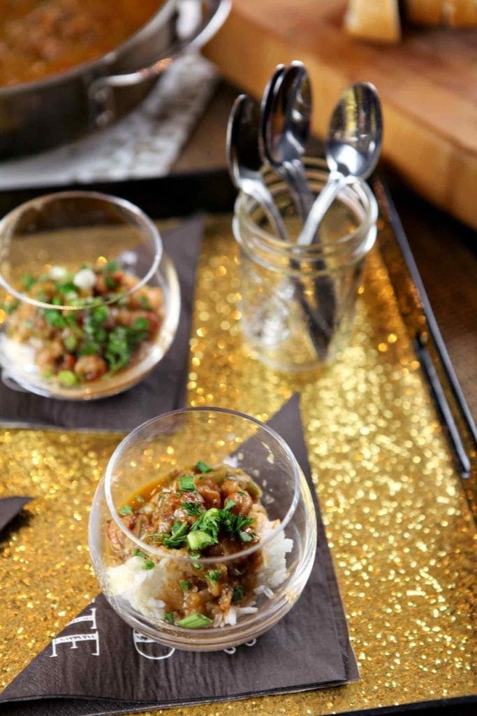 A shimmery gold tray holds clear glass cups holding crawfish etouffee over rice