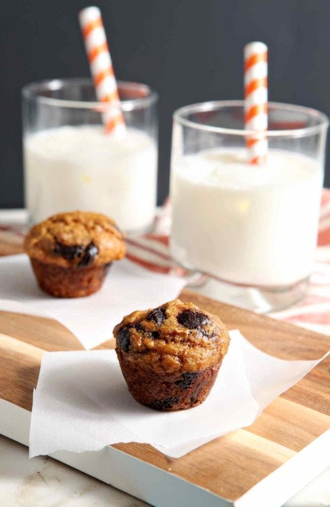 Mini Pumpkin Chip Muffins are served on a wooden serving platter with glasses of milk in the background