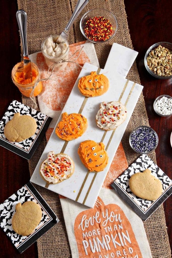 A marble tray surrounded by frosting and decorating items holds decorated pumpkin sugar cookies