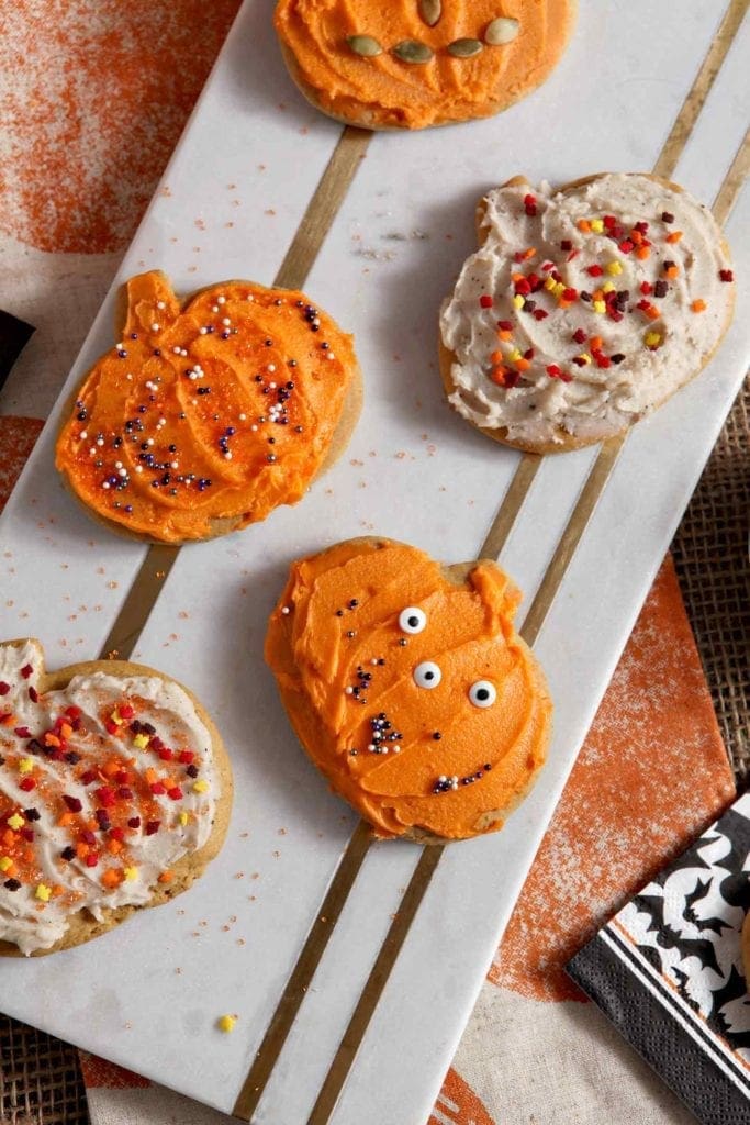 A marble tray holds several decorated Pumpkin Sugar Cookies with brown butter frosting