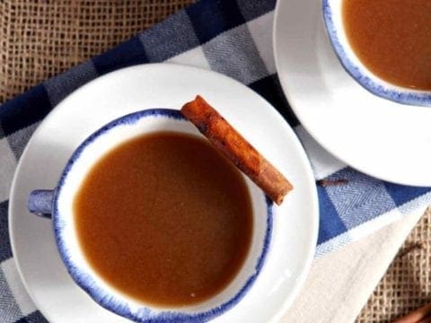 Two cups of Spiced Apple Cider, served in mugs with cinnamon sticks