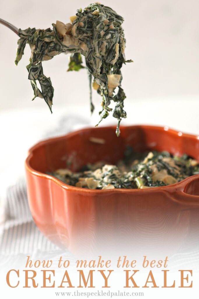 A spoon lifts a spoonful of Creamy Kale out of an orange serving dish that sits on a gray striped towel with the text 'how to make the best creamy kale'