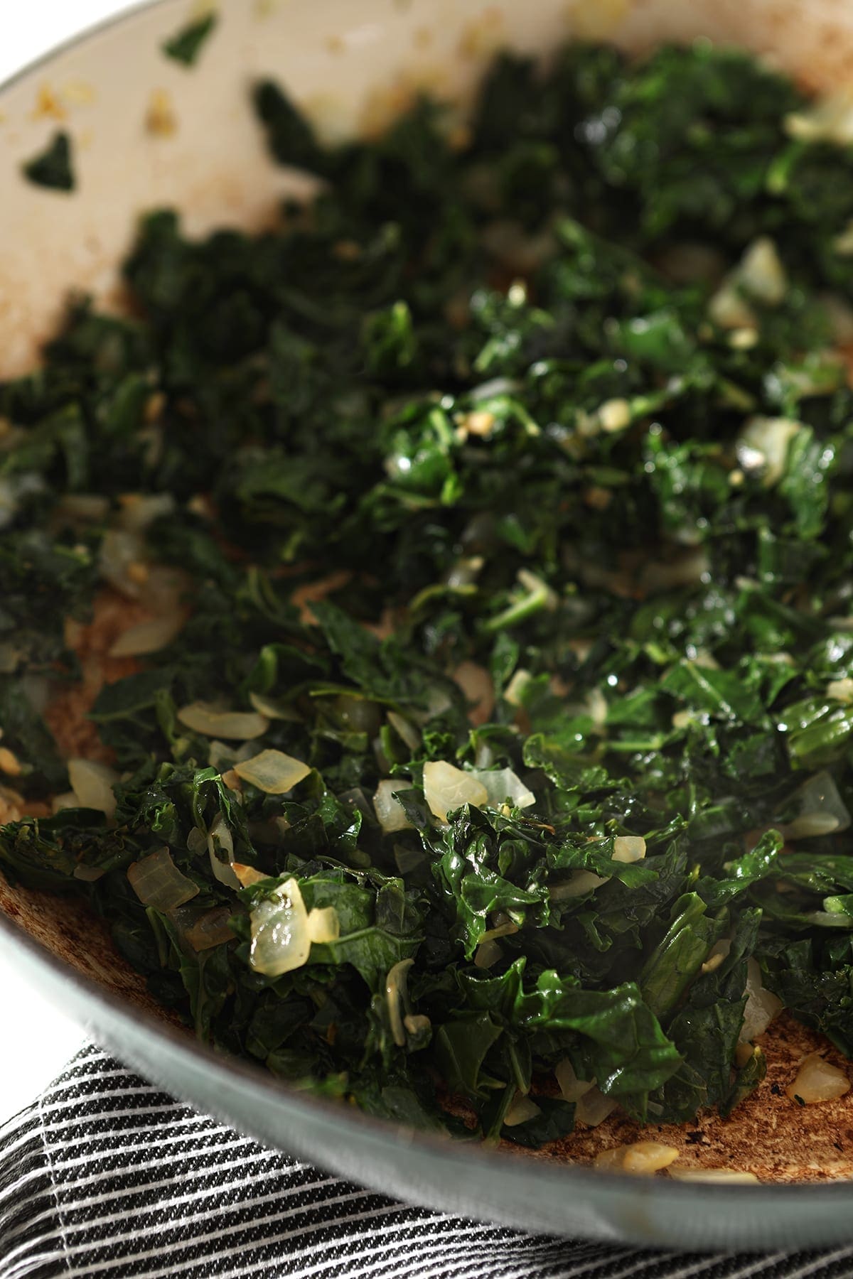 Close up of sauteed kale with onion and garlic in a pan