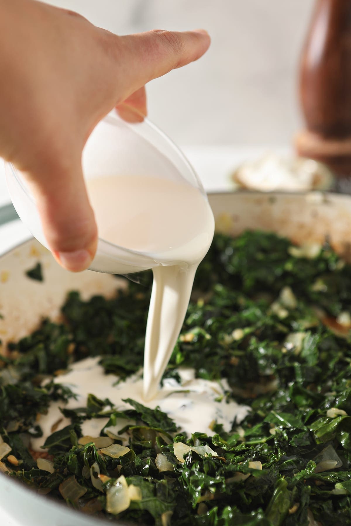 Cream pours on top of wilted kale in a pan