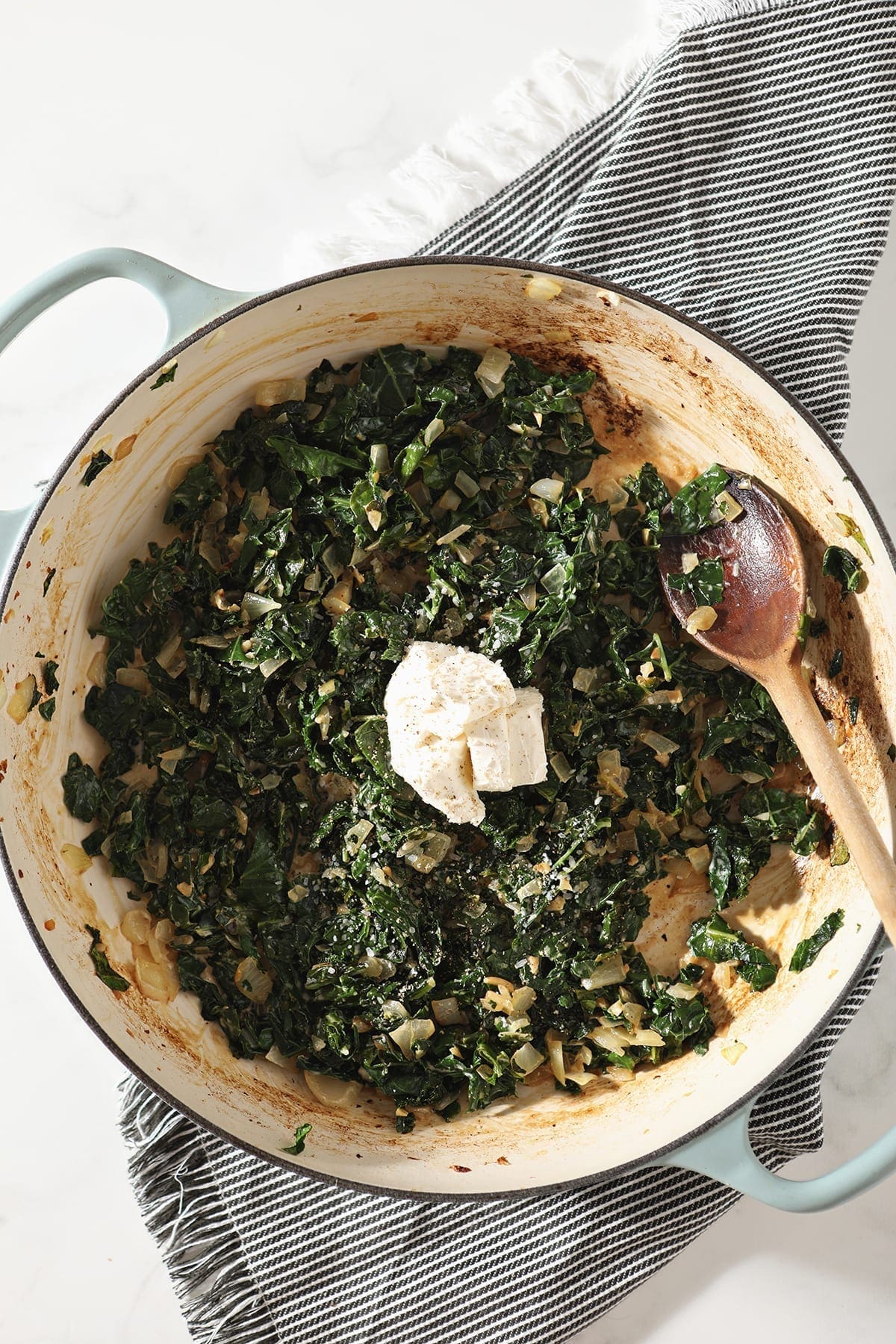 Cream cheese sits on top of wilted kale and cream in a pan, before stirring