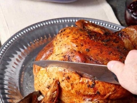 A whole roasted Browned Butter Sage Turkey is cut into with a knife.