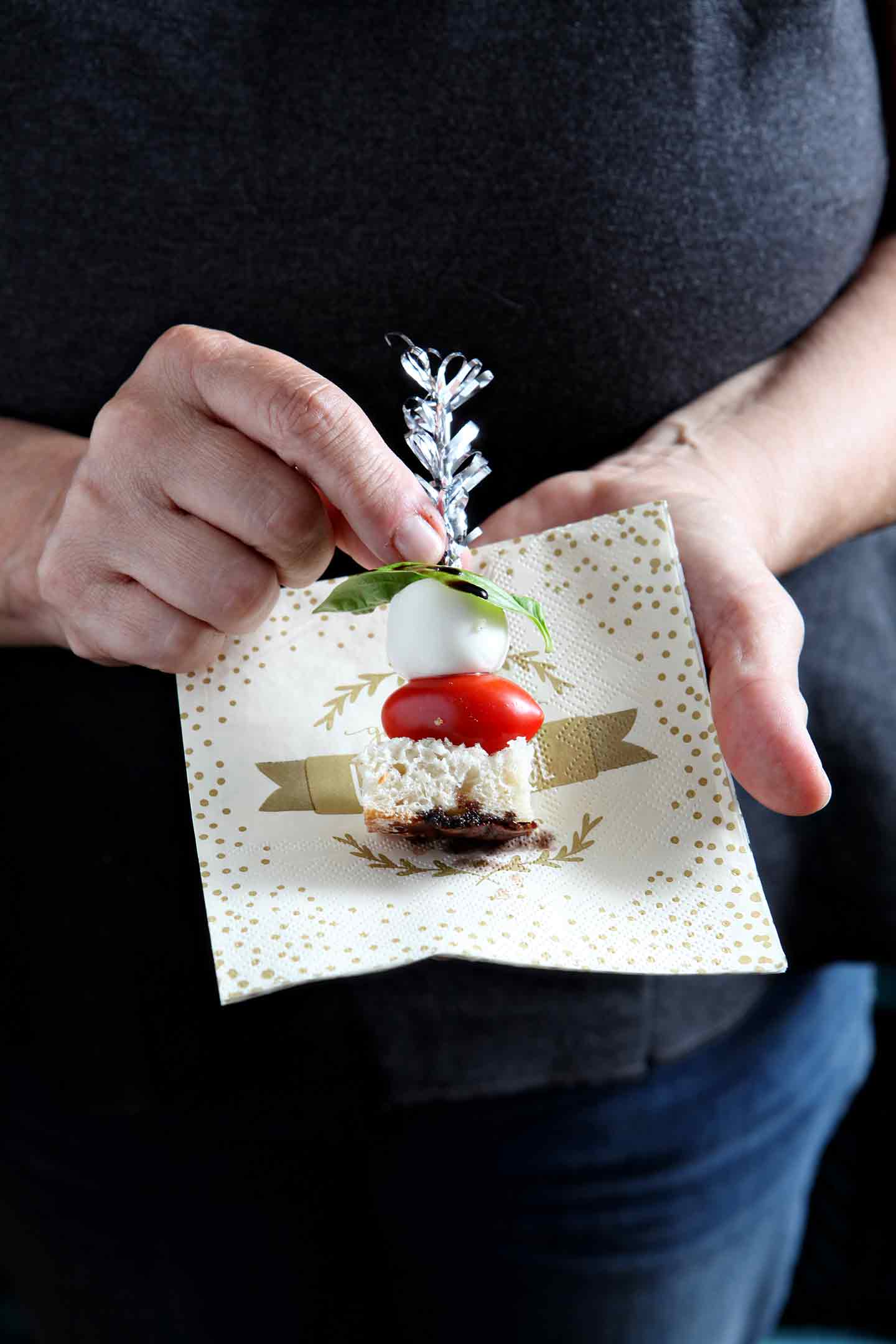 A woman holds a Caprese Skewer against a napkin before eating.