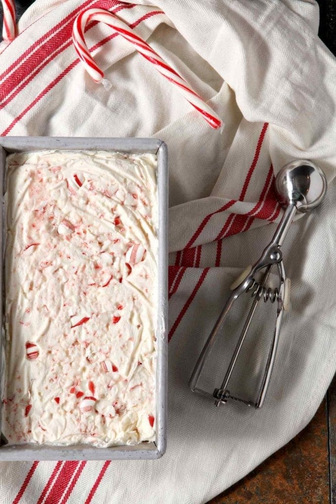 A loaf pan holds no churn peppermint ice cream, sitting on a red and white striped towel next to an ice cream scoop