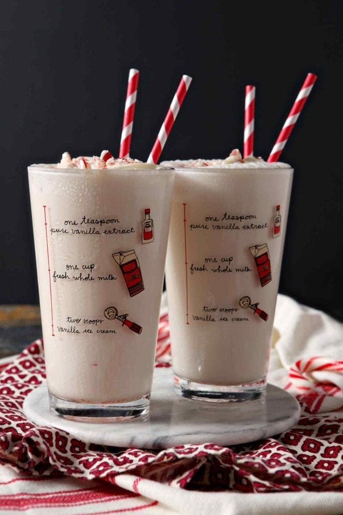 Two pint glasses with milkshake ingredient sketch on the side of them sitting on red patterned napkins and cloths with red striped straws