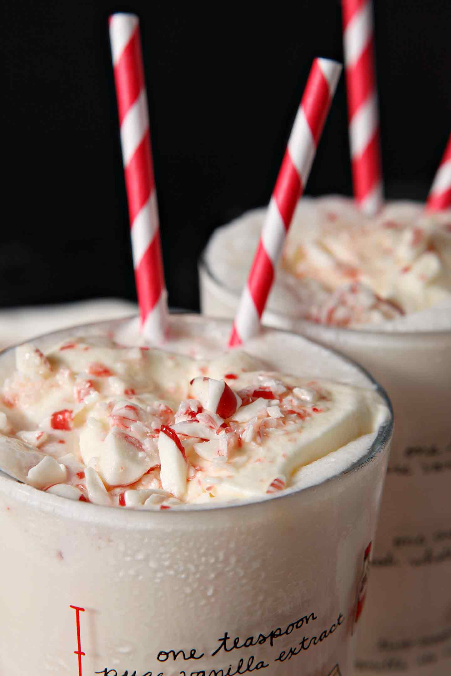 Close up of two pint glasses holding peppermint milkshakes garnished with whipped cream and peppermint pieces