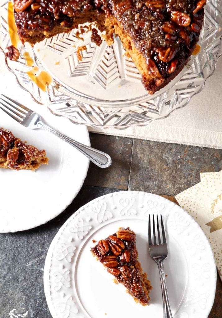 Two slices of Upside Down Pumpkin Cake on white plates, from above, next to the whole cake on a decorative glass plate