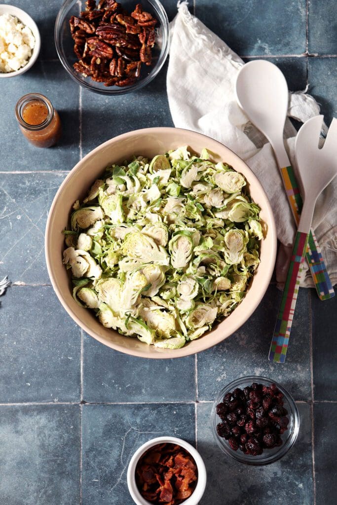 Ingredients to make a Brussels sprout salad in bowls on a dark blue tiled surface