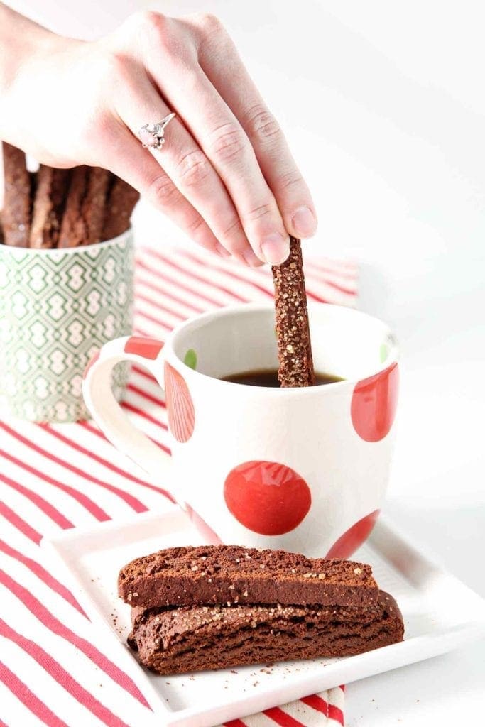 A woman dips a Chocolate Gingerbread Biscotti into a mug of coffee