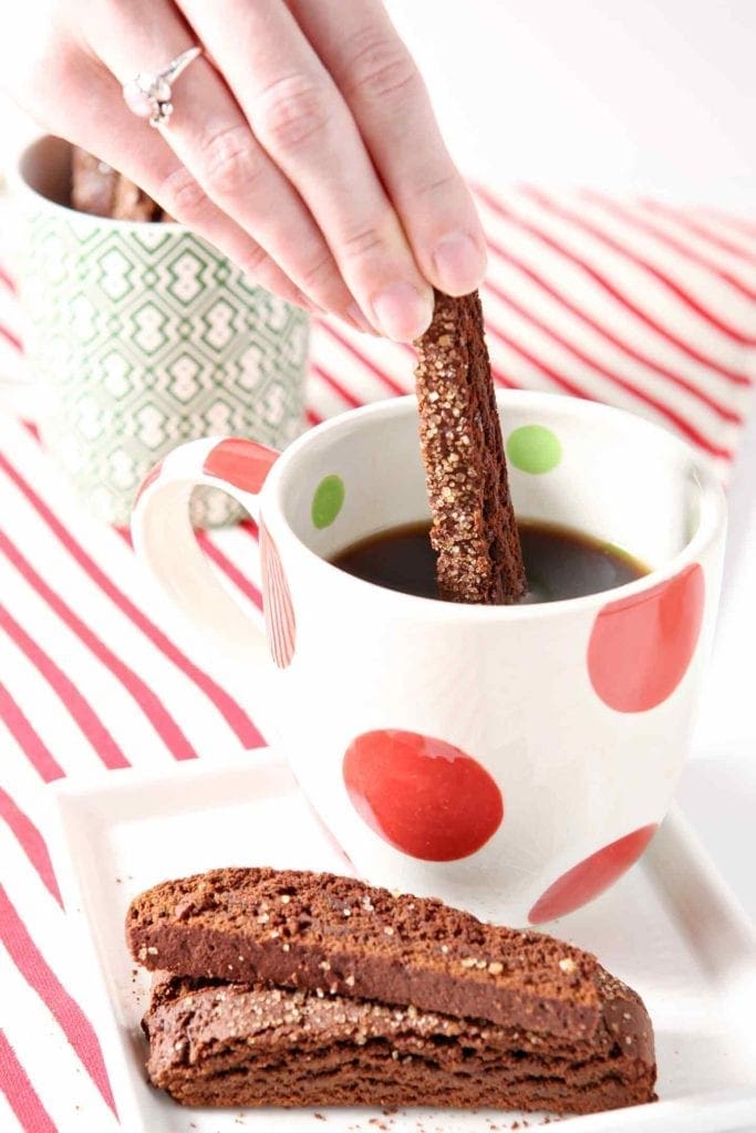 Hand dipping Gingerbread biscotti into red and green holiday mug