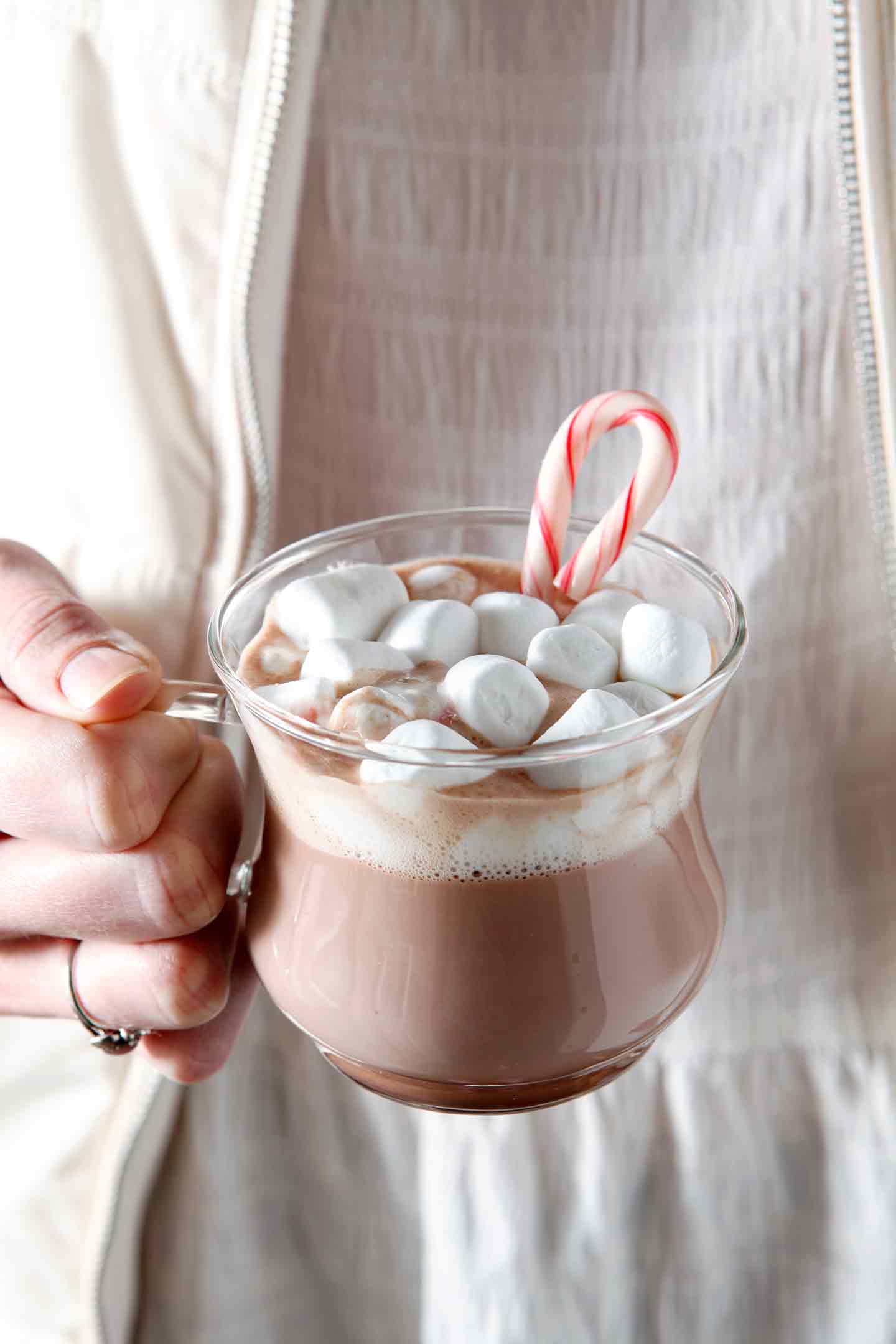 Hand holding mug of hot chocolate with marshmallows and candy cane 