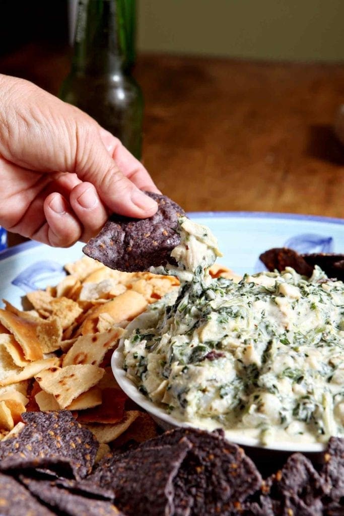 A person dips a tortilla chip into a bowl of Shrimp Spinach Artichoke Dip