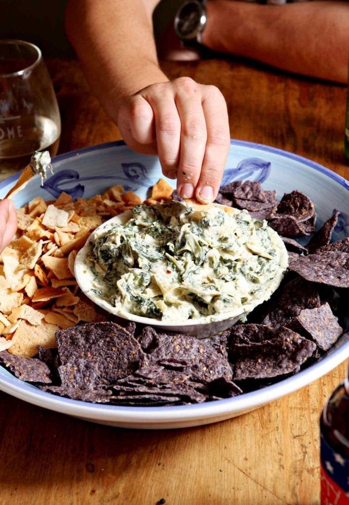 dipping a chip in spinach and artichoke dip 