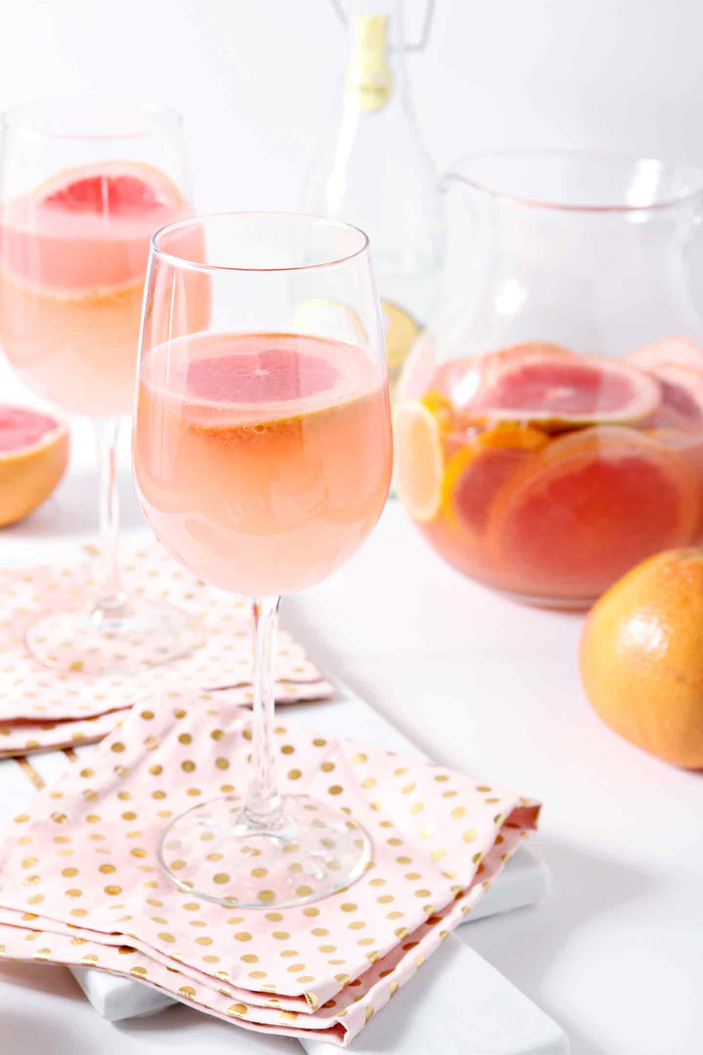 sparkling grapefruit sangria in a glass with a pitcher behind