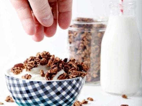 hand putting granola on yogurt