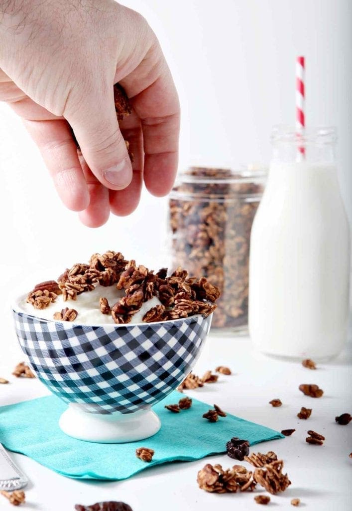 hand putting granola on yogurt