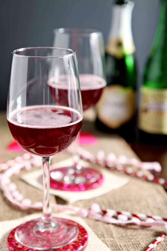 Two Framboise Champagne Cocktails sit on a decorate tabletop with the bottles of alcohol