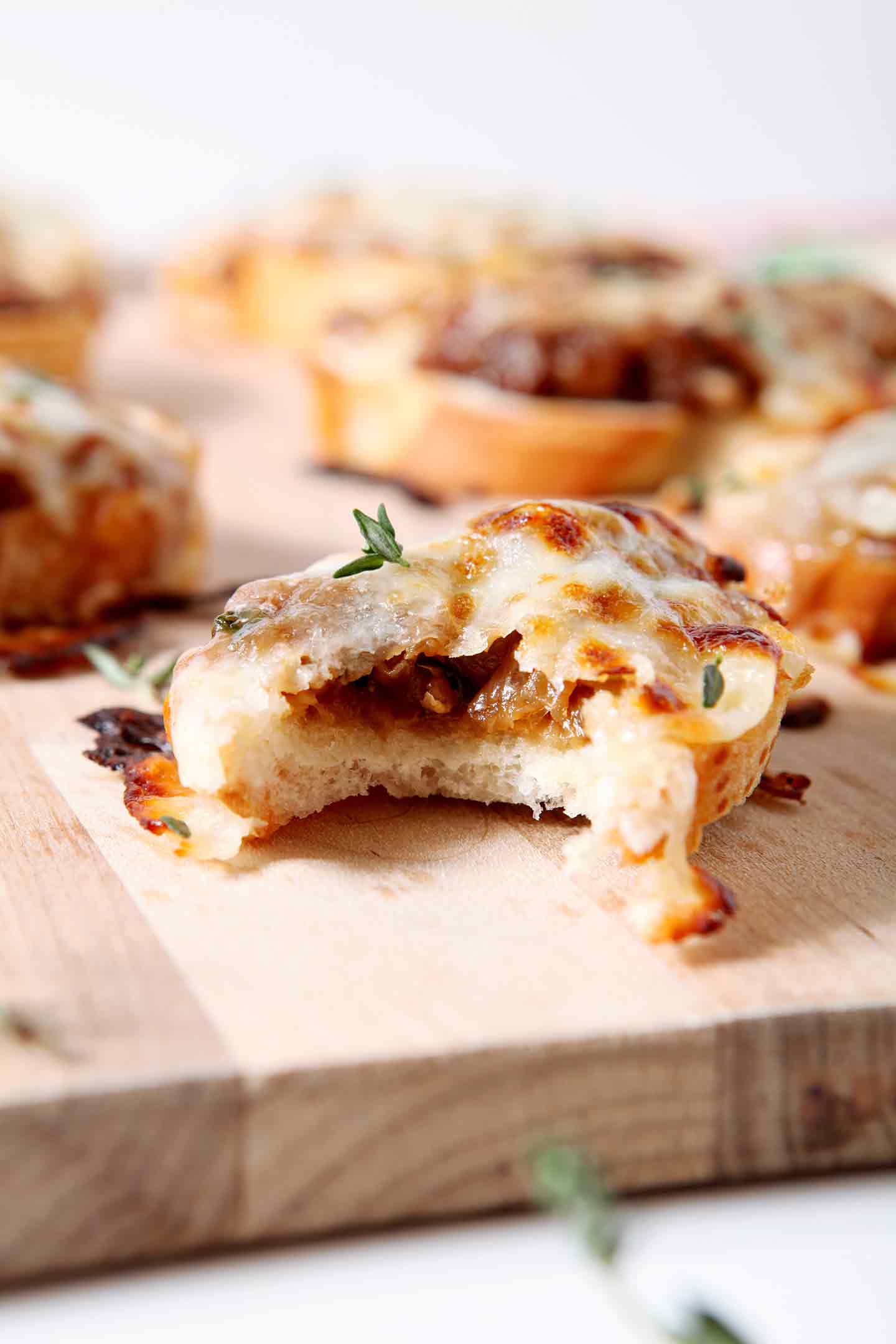 french onion bruschetta with a bite taken on a wood board