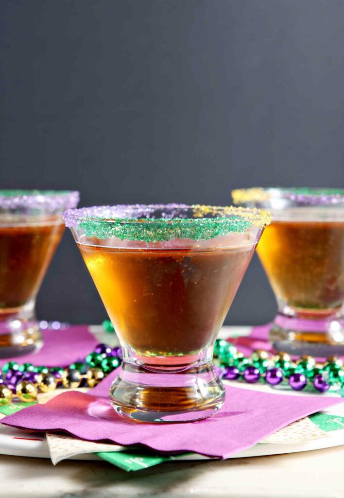 Three King Cake Martinis are served on purple napkins, surrounded by beads