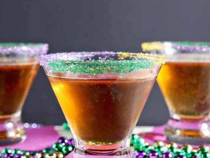 Three King Cake Martinis are served on purple napkins, surrounded by beads
