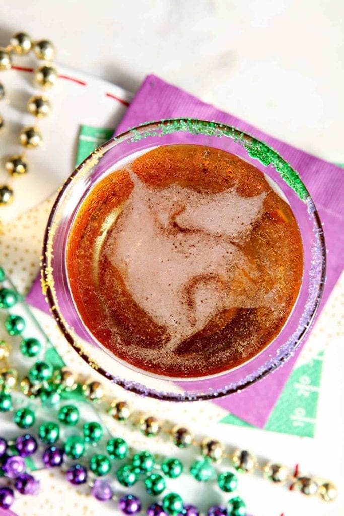 Close up showing a desert martini rimmed with purple, green and yellow sugar on a marble countertop