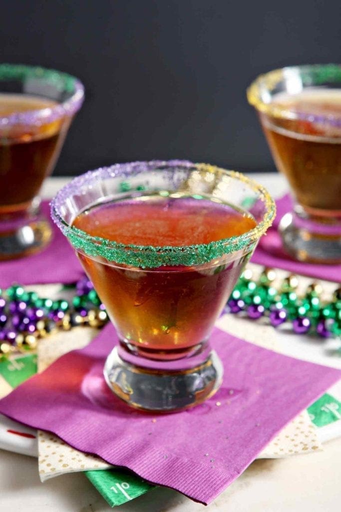 A king cake martini on a purple napkin, surrounded by festive mardi gras beads