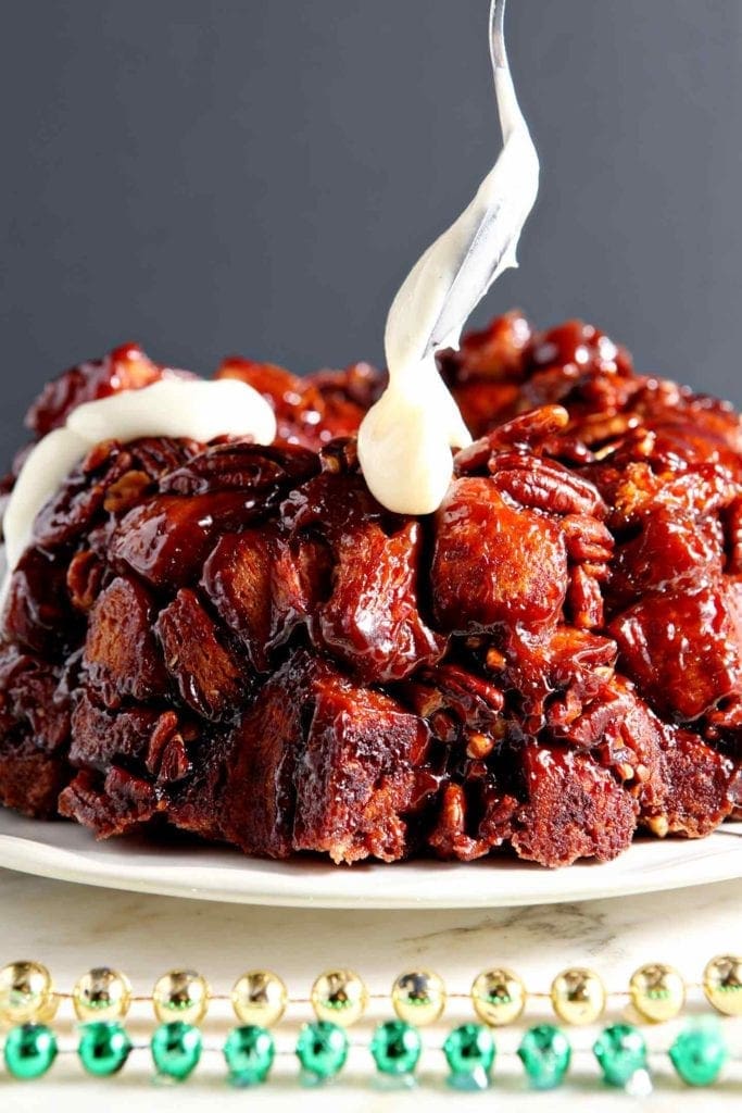 Cream cheese frosting is spread on top of monkey bread