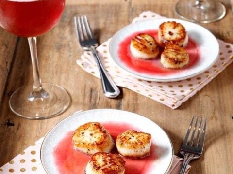 two white plates of seared scallops with two silver forks
