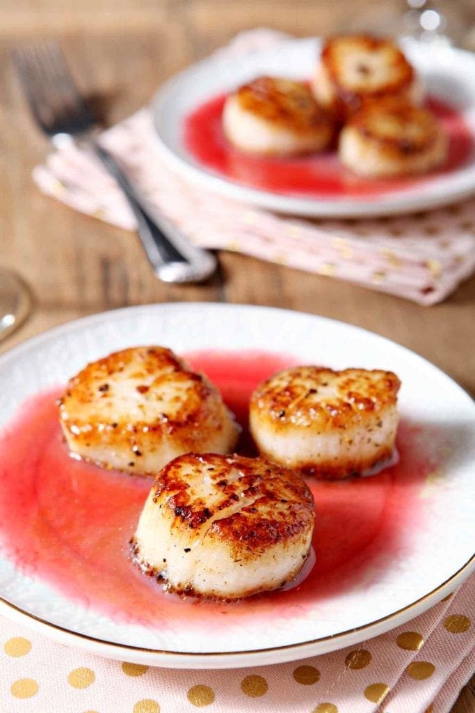 Close up of Seared Scallops with Raspberry Gastrique on a white plate